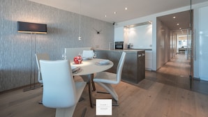 A modern kitchen with a central island, a dining area with white chairs, and a visible clock on the wall. - Marble Floor, full comfort sea view, parking incl. (Oostende)