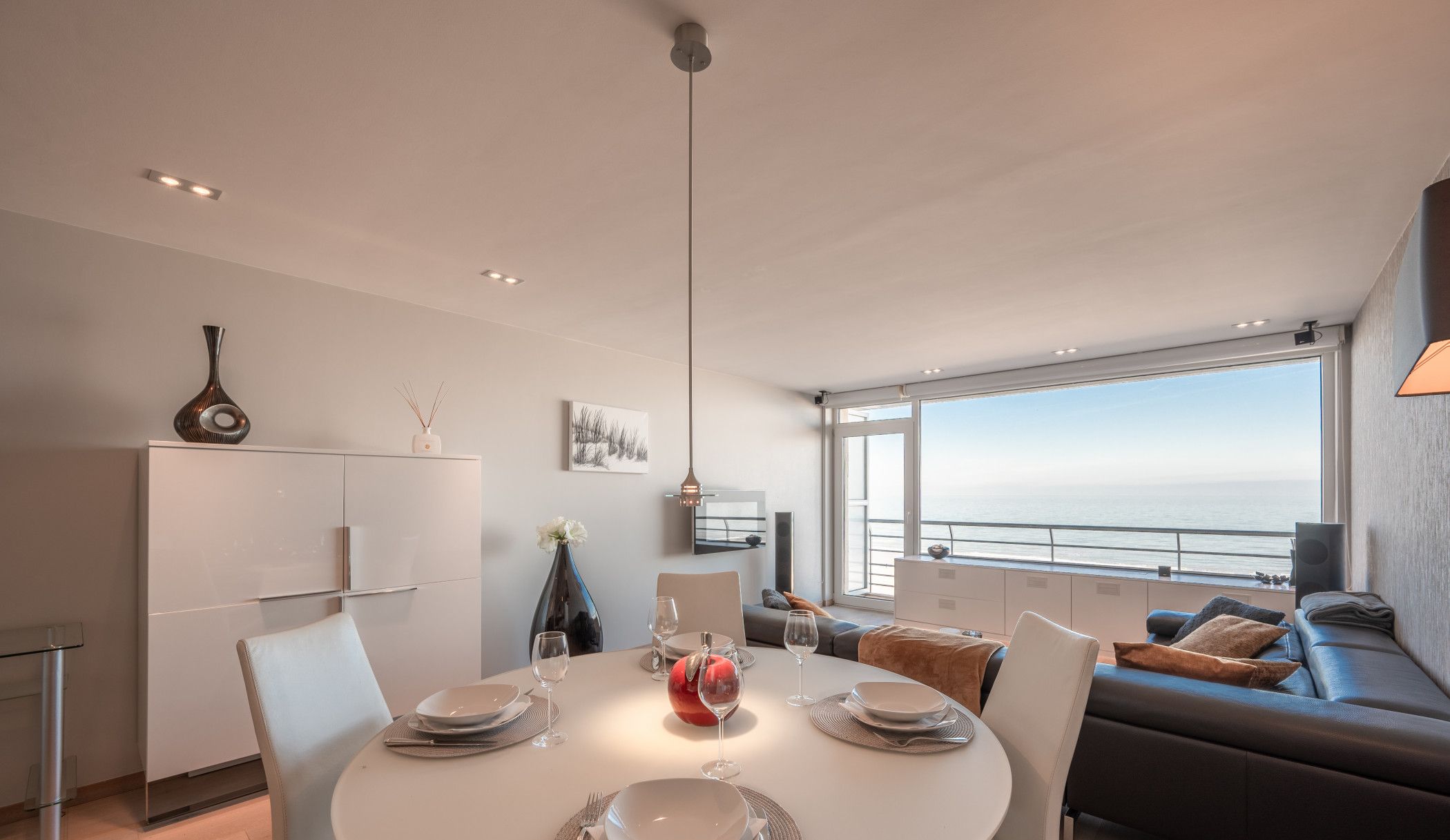 Ein moderner Essbereich mit einem runden Tisch für vier Personen, einer Couch und Blick aufs Meer.