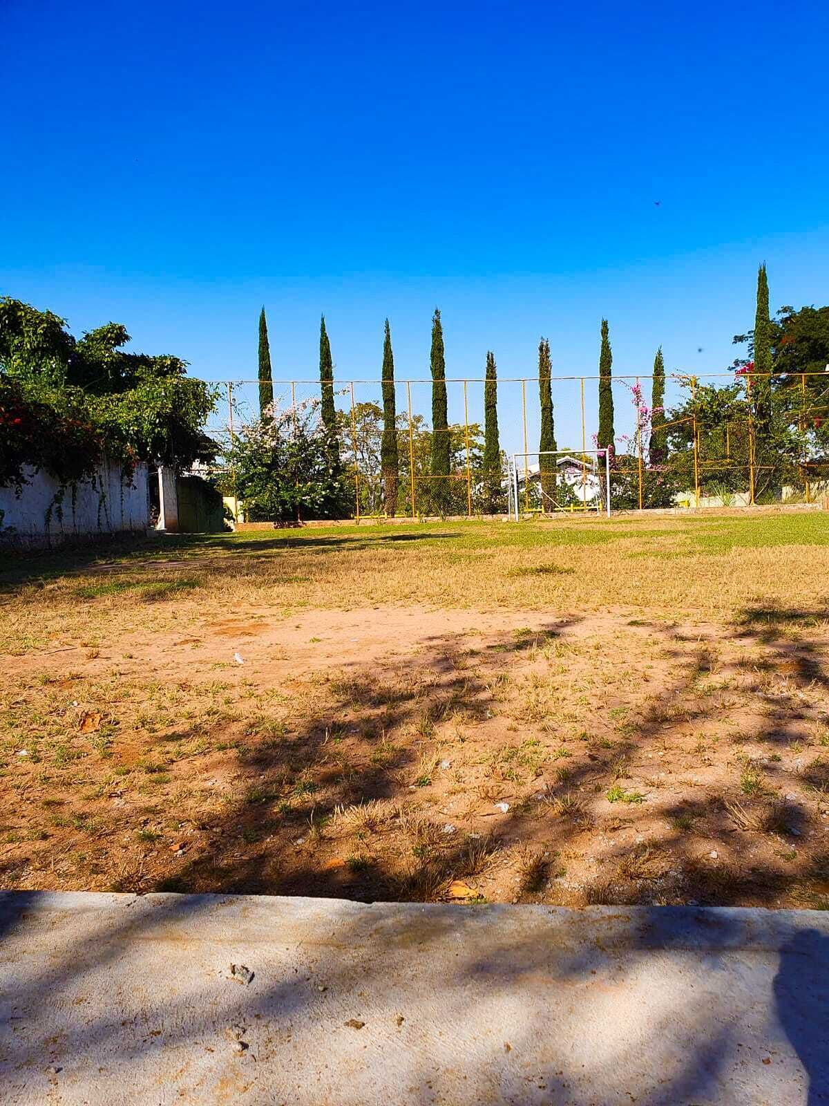 A grassy field with a goalpost, surrounded by tall trees and a white wall.