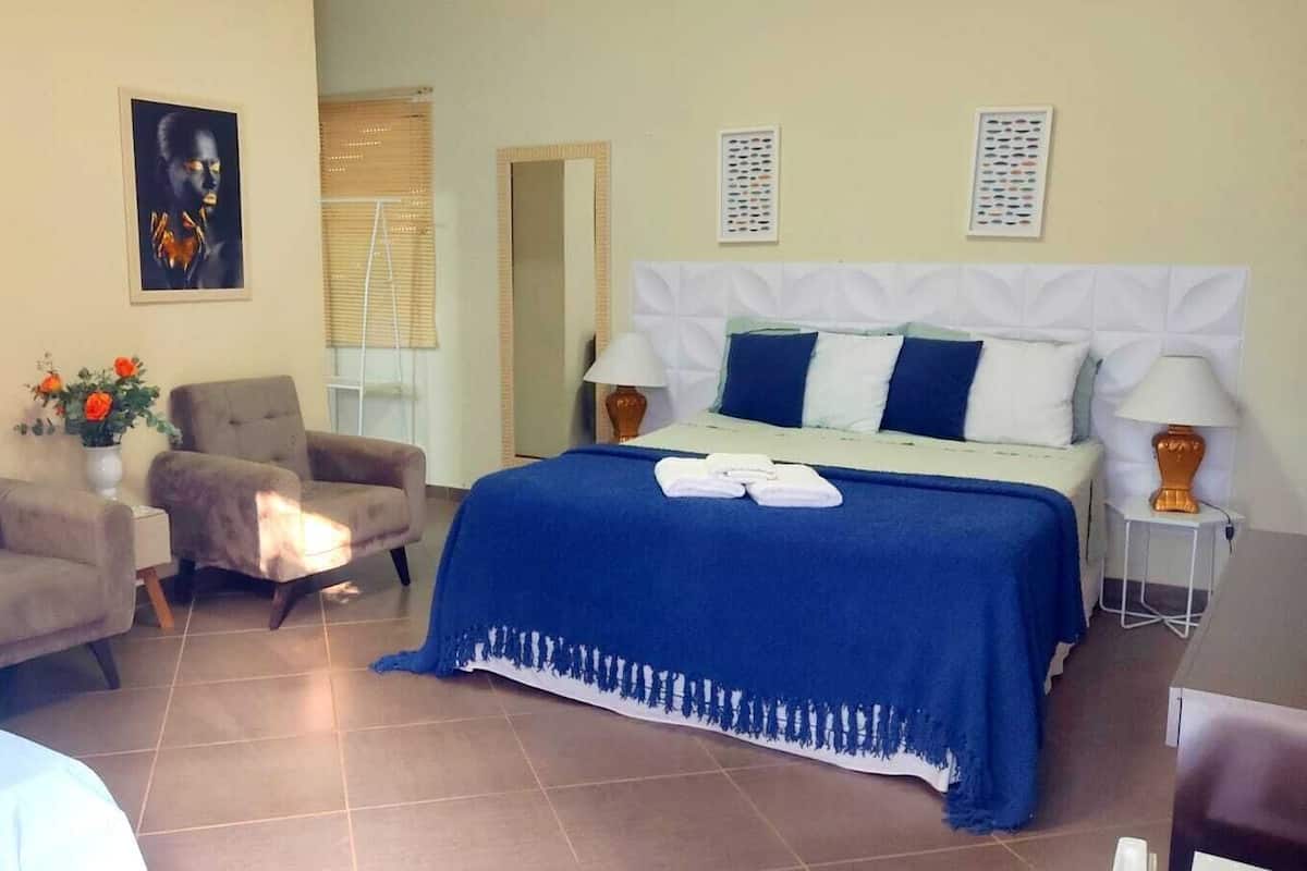 Un dormitorio con una cama, dos sillas, una mesita de noche, una lámpara y obras de arte en las paredes.