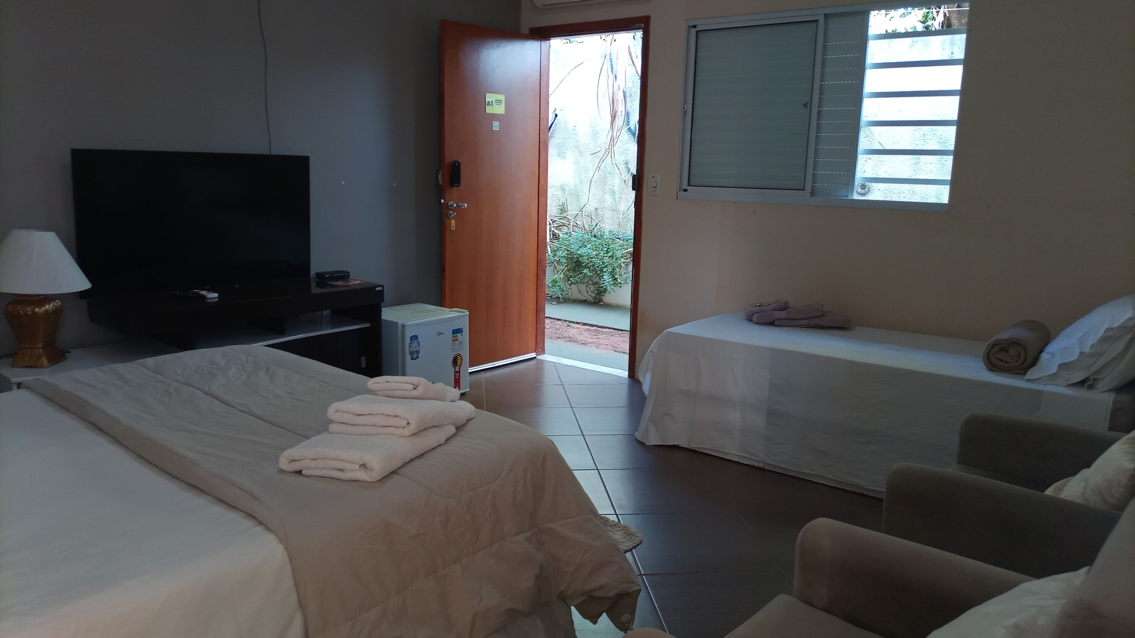 Habitació d'hotel amb dos llits, televisió, nevera petita i finestra amb persianes.