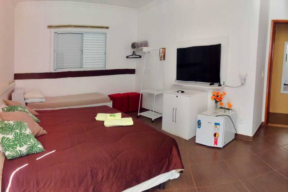 Habitación de hotel con cama, televisión, un mueble pequeño y ventana con persianas.