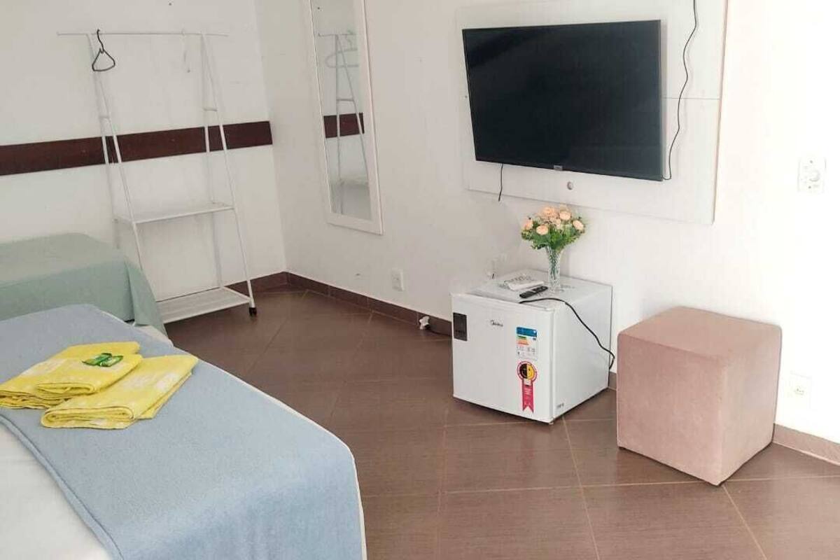 Una habitación de hotel con cama, televisión, una mesita con un florero y una mesita de noche.