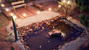 Een aangelegde tuin met een vijver, een houten terras en sfeerverlichting.
