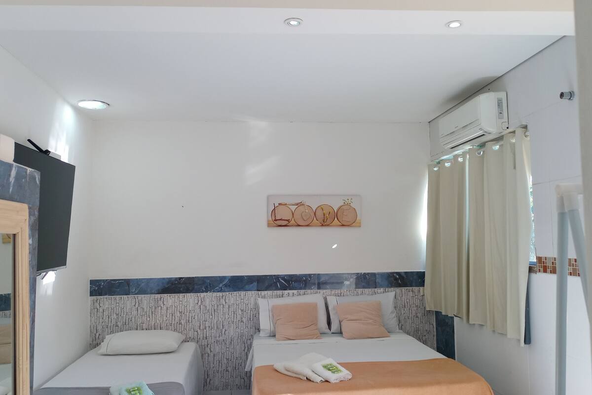 Habitación de hotel con cama, dos mesitas de noche, un aire acondicionado instalado en la pared y un adorno mural.