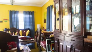 Un comedor con una mesa preparada para dos personas, un armario de madera con puertas de cristal y una pared amarilla con cortinas azules.