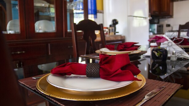 Una mesa de comedor dispuesta con un plato blanco, servilleta roja y plato con borde dorado.