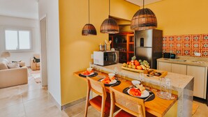 Une cuisine moderne avec un coin repas, comprenant une table en bois, des suspensions en osier et un panier de fruits.