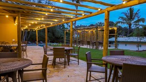 Un espace extérieur aménagé en terrasse, avec un sol en pierre, des meubles en osier et une pergola illuminée de guirlandes lumineuses.