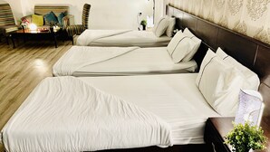 Et hotelværelse med tre senge, en sofa, en lampe og en lille plante.