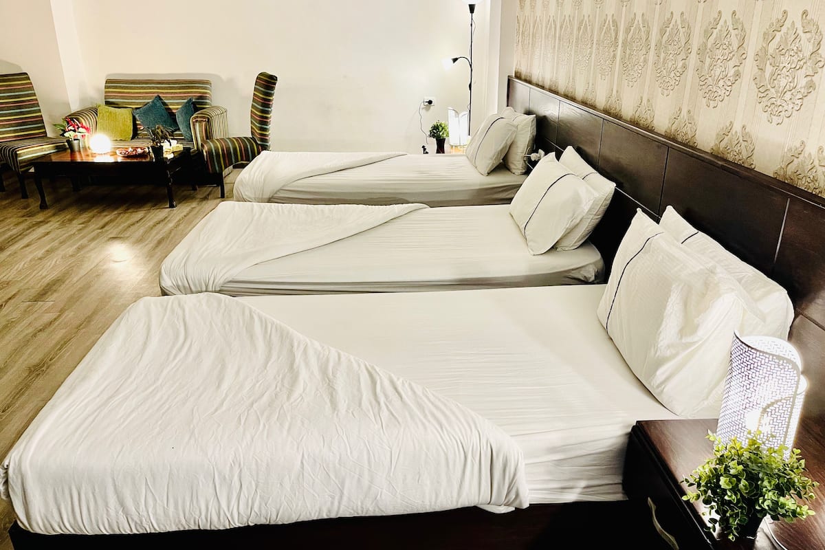 Une chambre d’hôtel avec trois lits, un canapé, une lampe et une petite plante.