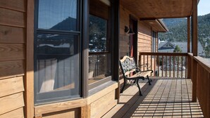 A wooden cabin with a balcony, large windows, and a view of a mountainous landscape.