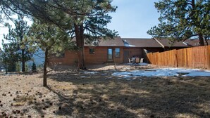 A wooden house with a fenced backyard, a small patio, and a tree in front.