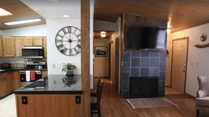A kitchen with wooden cabinets, a black countertop, a large wall clock, and a stone fireplace.