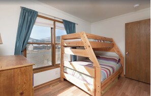 Una cama litera con estructura de madera, un escritorio y una ventana con cortinas.