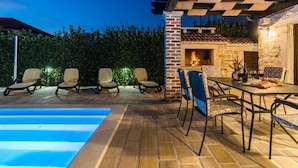 An outdoor patio with a swimming pool, seating area, and a fireplace.