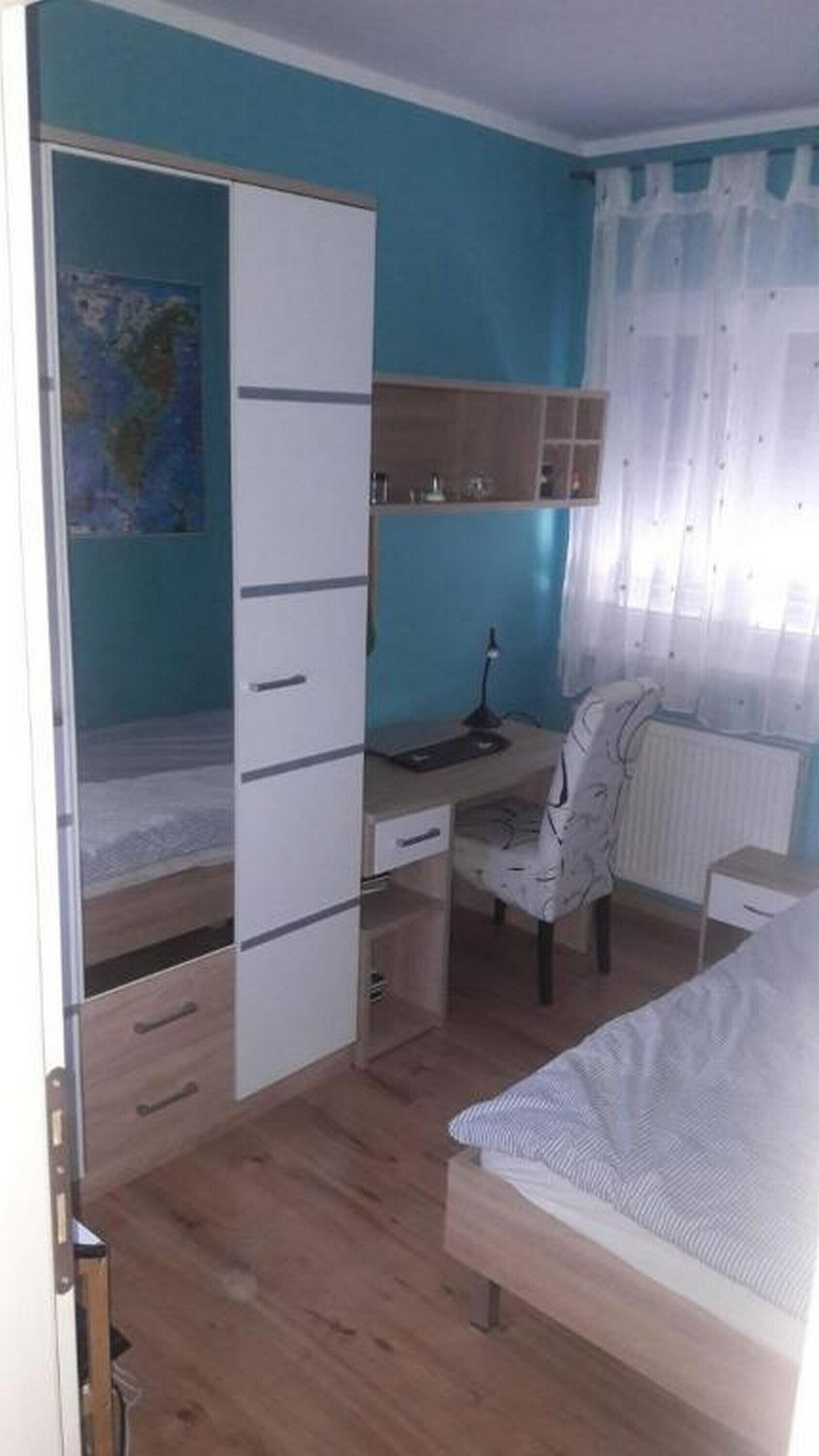 A bedroom with a bed, a desk, a chair, and a wardrobe.