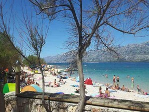 Ein Strand mit badenden und sonnenbadenden Menschen, Zelten und blauem Himmel.