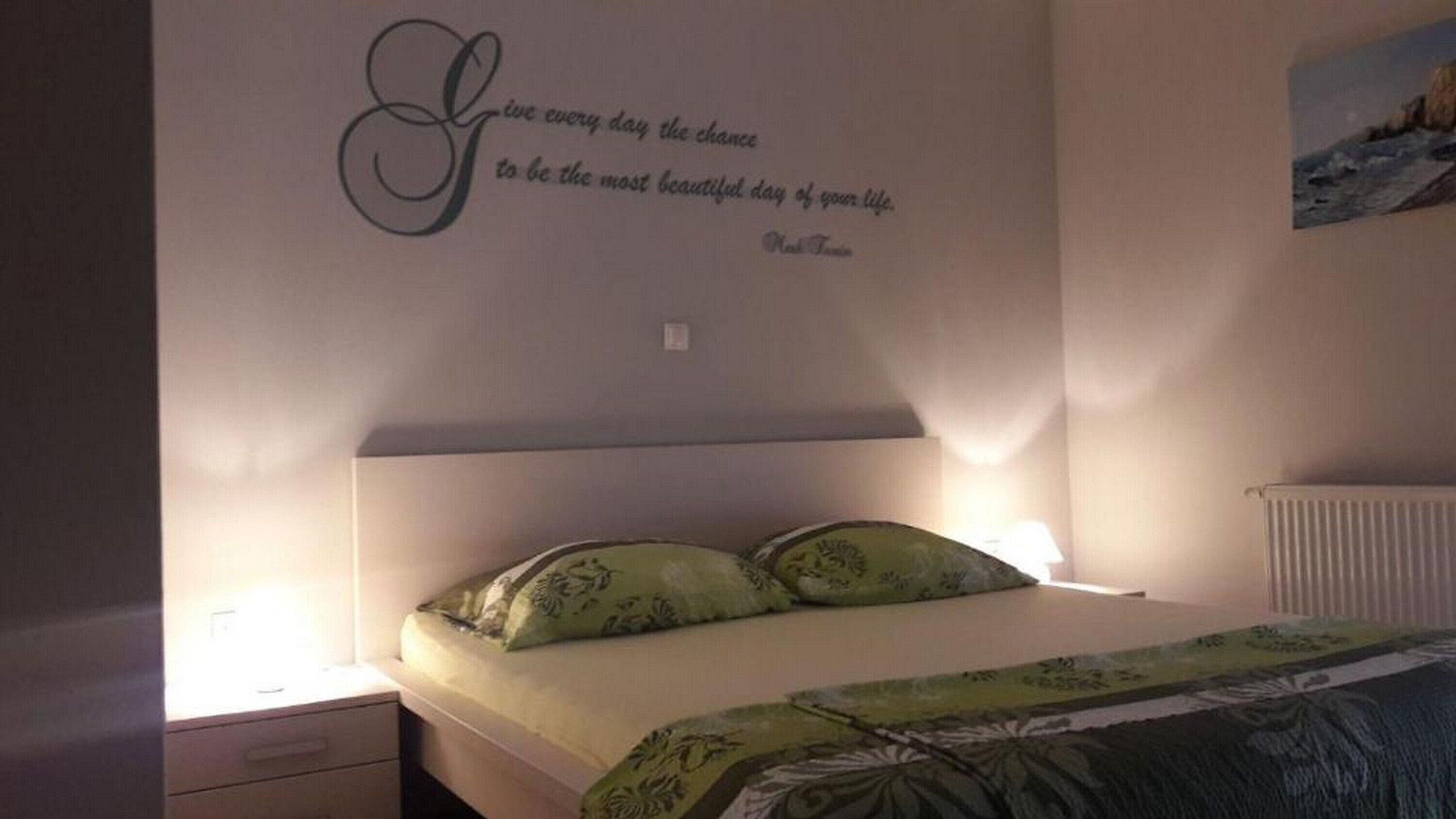Un dormitorio con cama, dos almohadas, una mesita de noche y una pared con una cita.