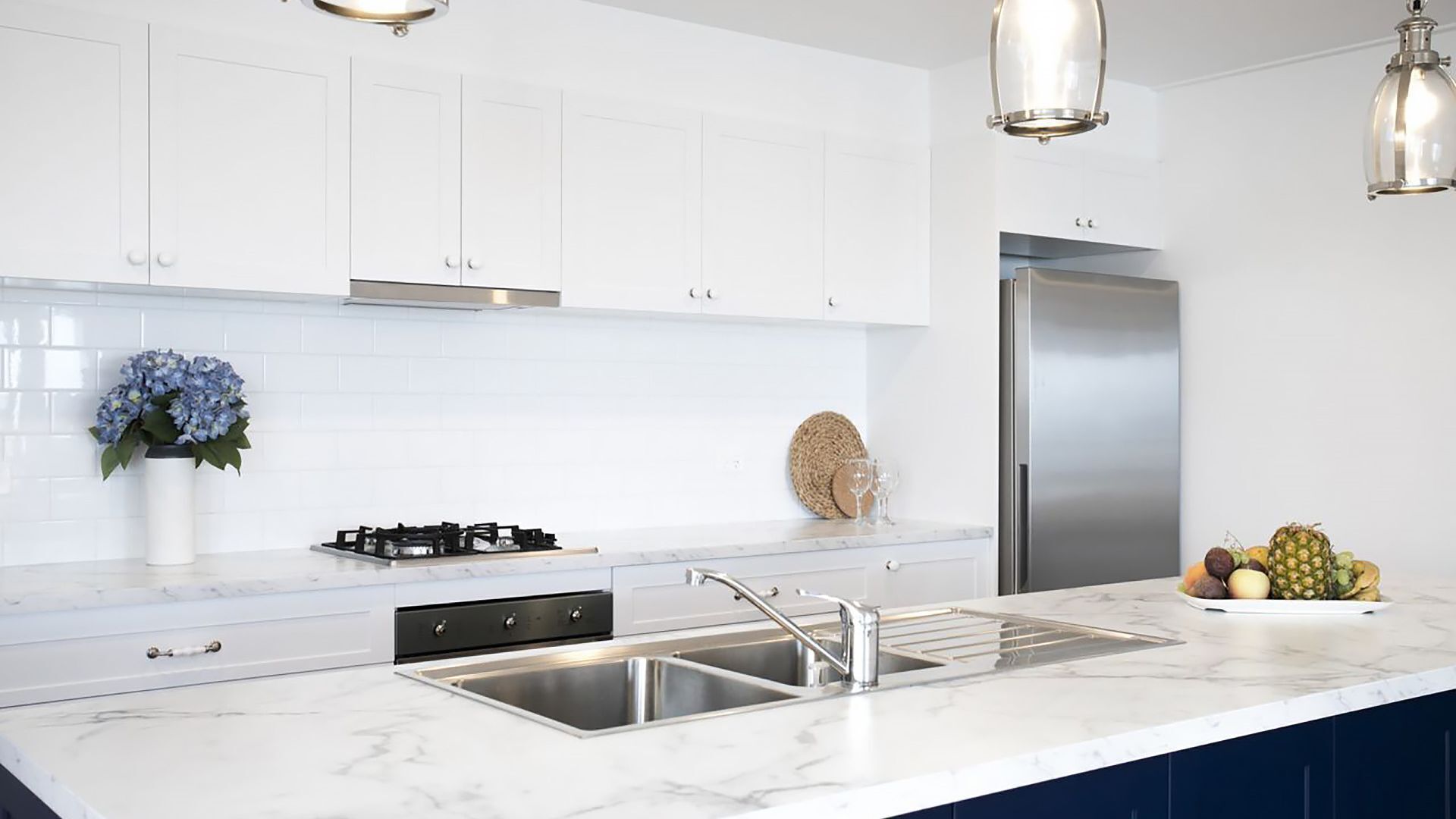 A modern kitchen with white cabinets, a stainless steel refrigerator, and a marble countertop.