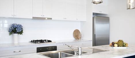 A modern kitchen with white cabinets, a stainless steel refrigerator, and a marble countertop.