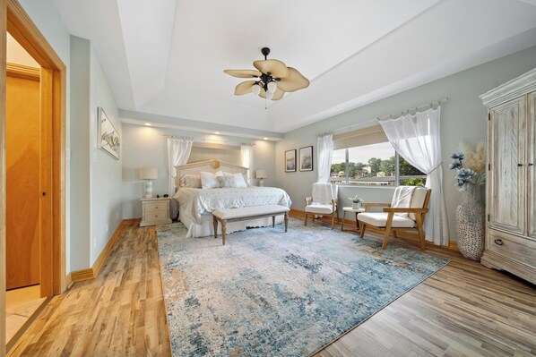 A bedroom with a bed, bedside tables, a chair, a large window, and a ceiling fan. - Brownstone - Amazing 3,600 SF home SLEEPS 18 --Game room--HOT TUB (Sunrise Beach)
