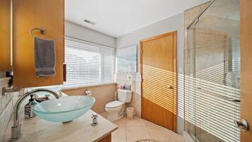 A modern bathroom with a glass bowl sink, a toilet, and a shower with a glass door.