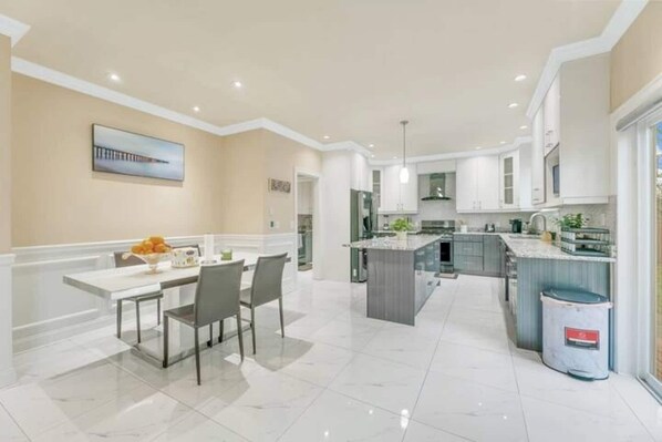 A modern kitchen with a central island, white cabinetry, and a dining area with a table and chairs. - Luxe Puget Sound Private Getaway in Burien! (Burien)