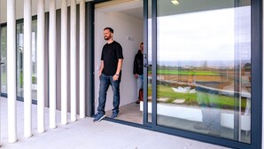 Een modern gebouwde entree met een glazen deur en zicht op een groen landschap door het glas.