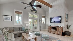 A spacious living room with a large ceiling fan, a television, and a wooden entertainment center. - Sunset Bay 111 ST (Port Aransas)