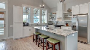 A modern kitchen with a large island, white cabinetry, and a stainless steel refrigerator. - Sunset Bay 111 ST (Port Aransas)