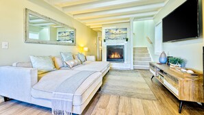 Una sala de estar moderna con chimenea, un sofá, un televisor y una escalera que sube a otro nivel.
