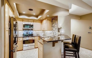 A modern kitchen with a central island, built-in appliances, and a stone backsplash.