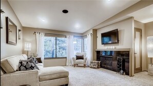 A living room with a beige sofa, a patterned armchair, a fireplace, and a TV mounted above it.