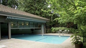 A swimming pool with a covered area, surrounded by greenery and outdoor seating.