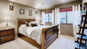 A bedroom with a wooden bed, bedside tables, a window with curtains, and a ladder against the wall.