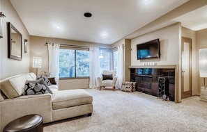 A living room with a beige sofa, a patterned armchair, a fireplace, and a TV mounted above it.