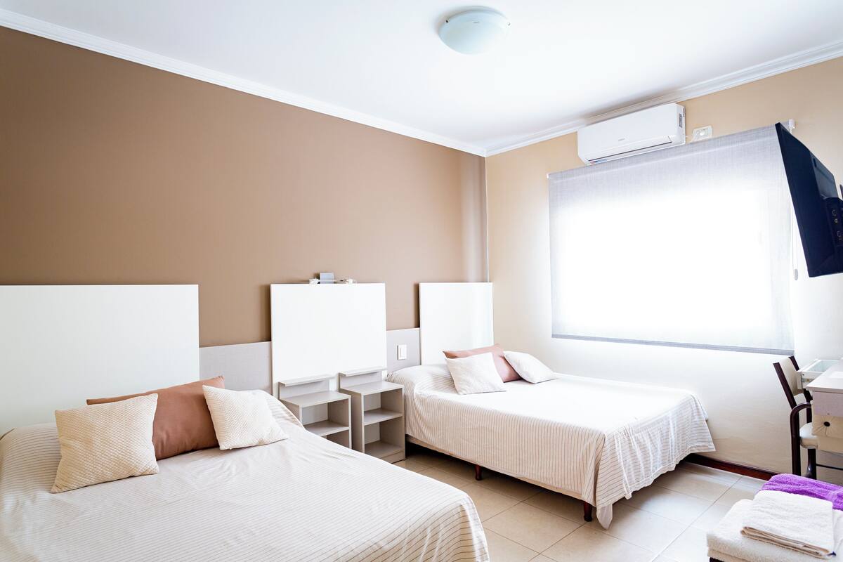 Une chambre d’hôtel avec deux lits, un bureau, une chaise et une fenêtre avec des rideaux.