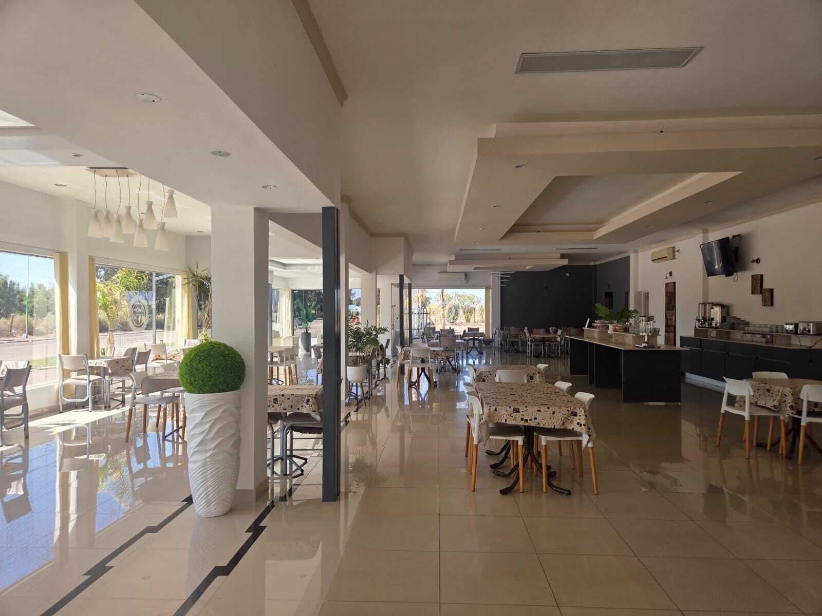 A spacious hotel lobby with multiple dining areas, a kitchen, and a large window providing a view of the outdoors.