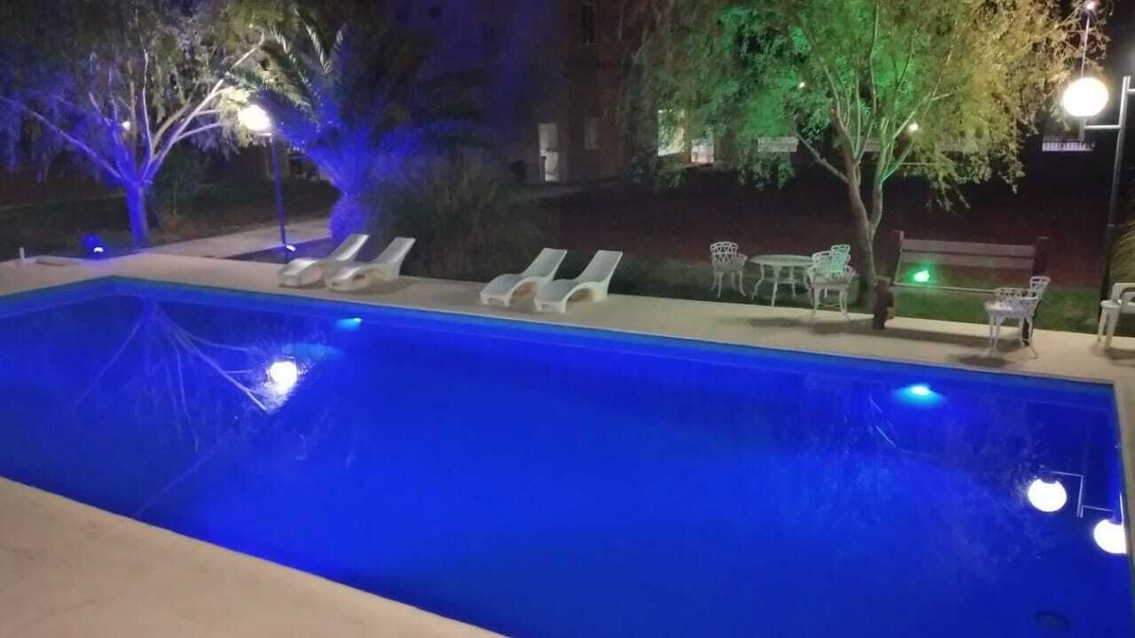 Una piscina con sillones de descanso y un área de patio por la noche.