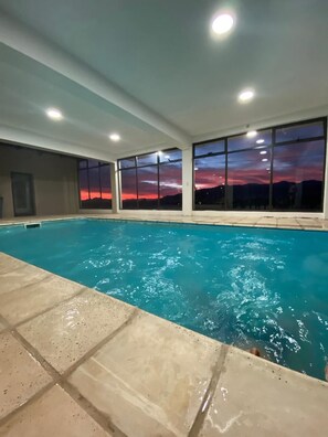 Une piscine intérieure à l’eau claire, entourée de grandes fenêtres qui offrent une vue sur le coucher du soleil.