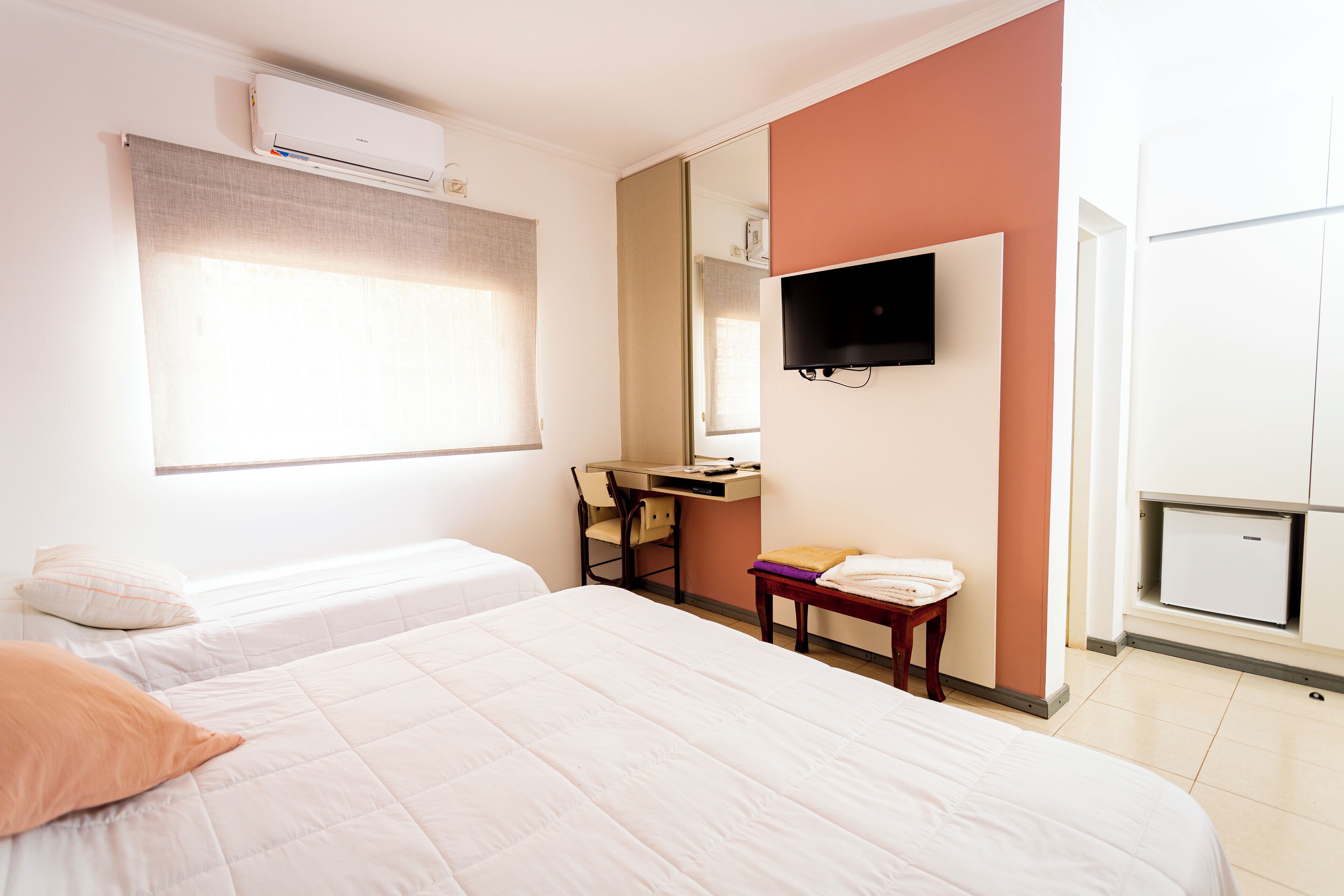 A hotel room with a bed, a desk, a chair, a TV, and a wardrobe.