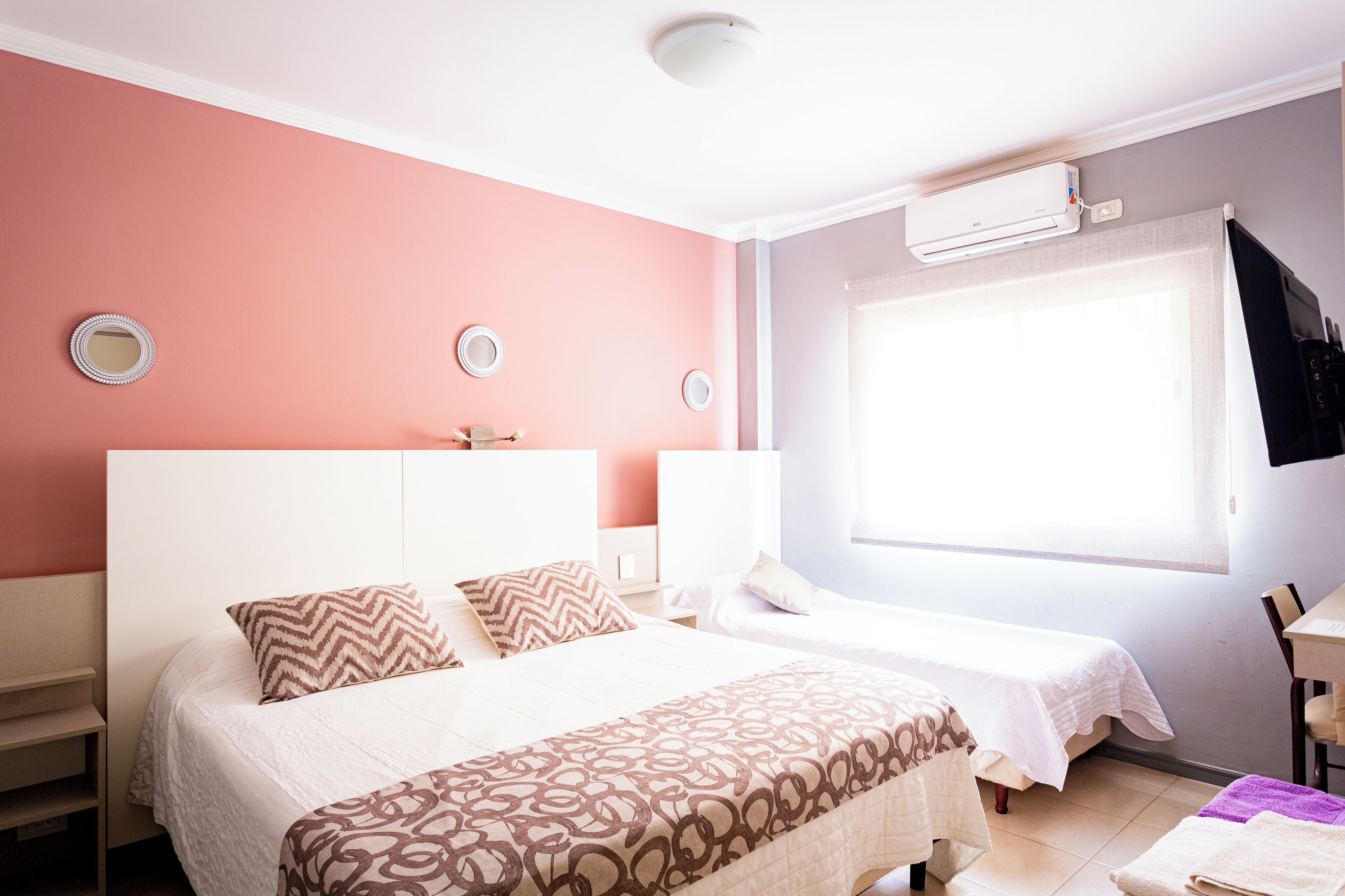 A hotel room with a large bed, a smaller bed, a desk, and a window with blinds.