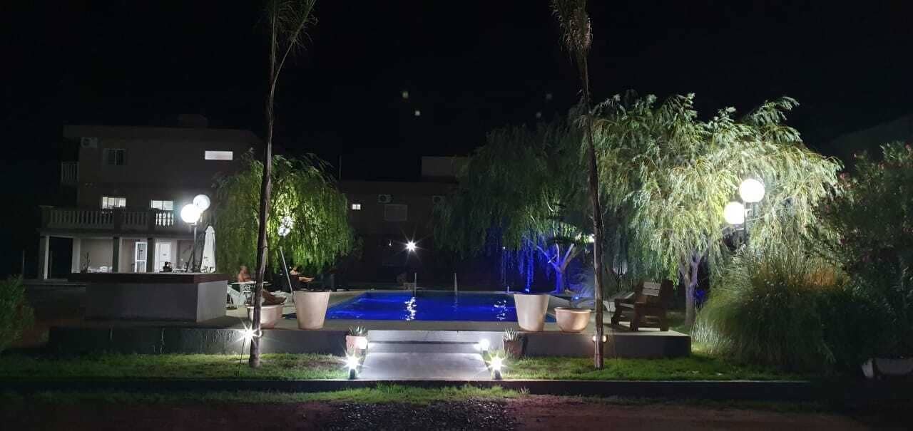 A swimming pool at night with surrounding trees and a building in the background.