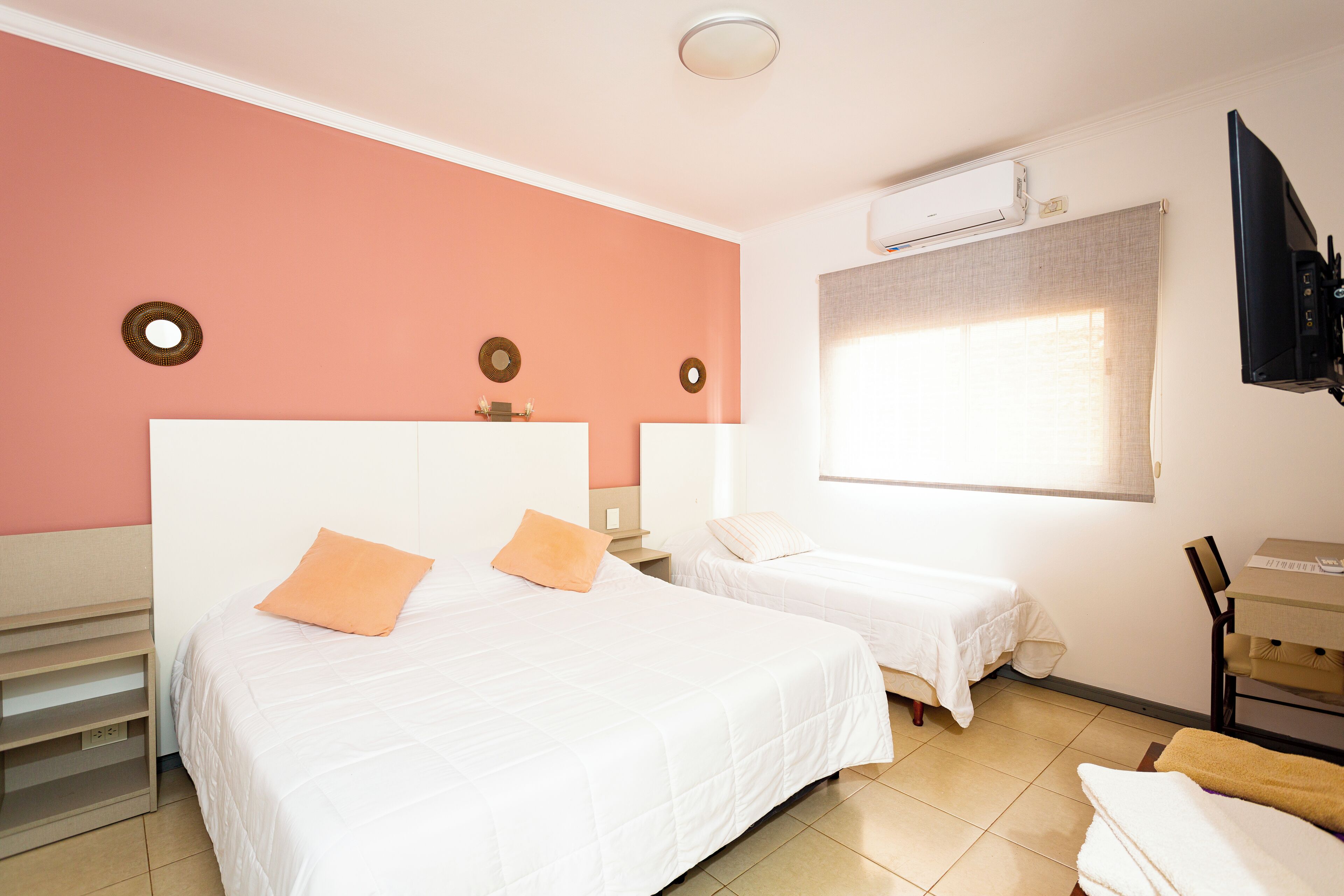 Una habitación de hotel con dos camas, televisión y ventana con cortinas.
