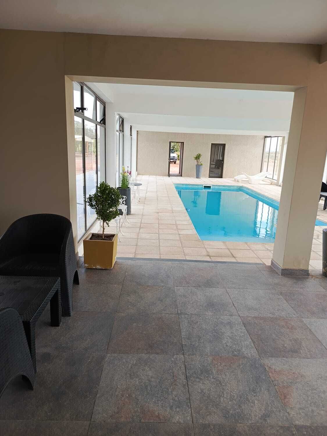 An indoor swimming pool with a view of the outside, a chair, and a potted plant.