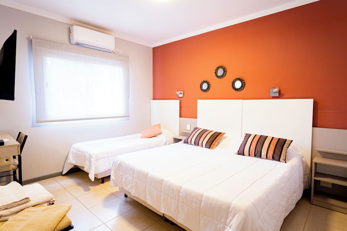Une chambre d’hôtel avec deux lits, une fenêtre avec des rideaux, un appareil de climatisation et un mur orné de miroirs décoratifs.