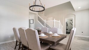 Comedor con mesa de madera y sillas tapizadas, candelabro y una escalera al fondo.