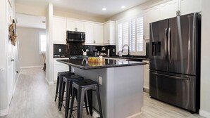 Una cocina moderna con armarios blancos, un refrigerador negro, un microondas y una isla grande con taburetes de bar.