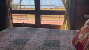 Una habitación con una cama grande, vistas a un lago a través de una ventana y una terraza de madera afuera.